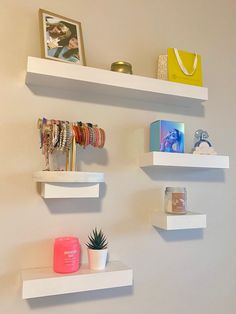 three white floating shelves with bracelets and other items on them, along with a cactus