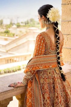 a woman in an orange and gold dress sitting on a stone ledge with her back turned to the camera