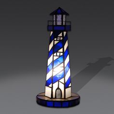 a blue and white lighthouse shaped lamp on a gray background with shadow from the light