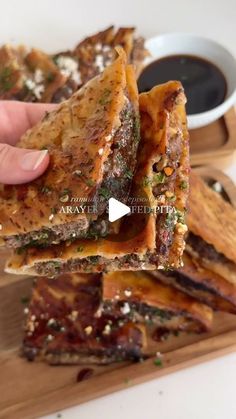 someone is holding up some food on a cutting board with dipping sauce in the background