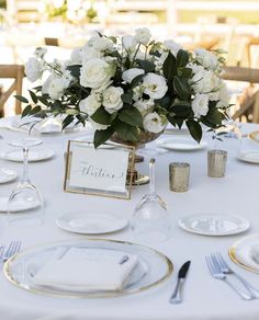 a table set with white flowers and place settings