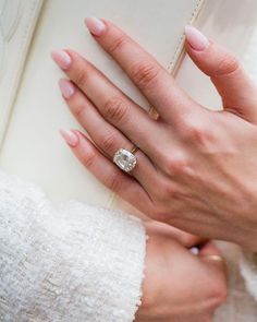 a woman's hand holding an open book with a diamond ring on her finger