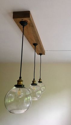 three clear glass globes hanging from a wooden beam in a room with white walls