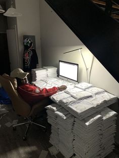 a pile of papers sitting on top of a desk next to a computer monitor and lamp