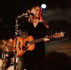 a woman holding a guitar and singing into a microphone