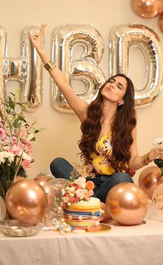 a woman sitting at a table with balloons and flowers in front of her, surrounded by large letters