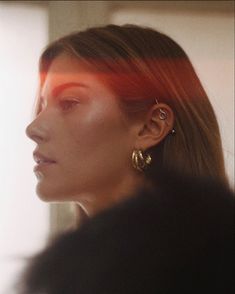 a woman with red hair and gold hoop earrings looking off to the side in front of a window