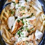 a blue bowl filled with pasta covered in sauce and chicken breast pieces on top of it