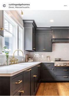 a kitchen with dark gray cabinets and white counter tops, gold pulls on the handles