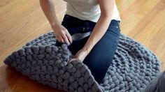 a woman sitting on top of a knitted dog bed with her legs tucked under the blanket