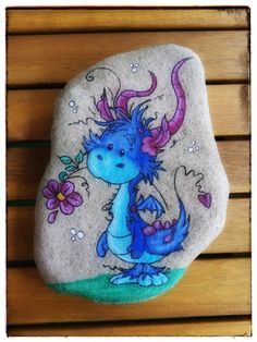 a rock with a blue dragon painted on it sitting on a wooden bench next to flowers