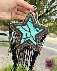 a hand holding up a blue and black star ornament with fringes on it