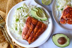 two white plates topped with salmon and coleslaw next to an avocado