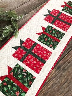 a quilted table runner with red and green christmas decorations on it, along with a wreath