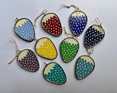 six different colored polka dots are hanging from hooks on a white surface, each with an oval shaped ornament in the center