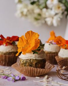 three cupcakes with white frosting and orange flowers on top are sitting on a table