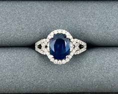 a blue and white diamond ring sitting on top of a gray cloth covered cushioned surface