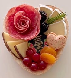 an arrangement of cheese, fruit and meats in a heart shaped bowl with a flower