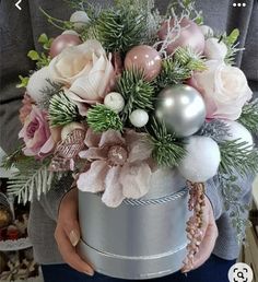 a woman holding a silver bucket with flowers and ornaments in it's centerpiece