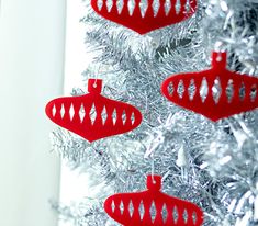 three red ornaments hanging from a silver christmas tree