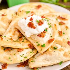 a white plate topped with quesadillas covered in sour cream and garnished with bacon