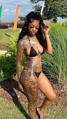 a woman with tattoos on her body standing in the grass and posing for a photo