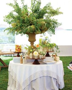 a table topped with lots of flowers and greenery next to an umbrella on top of a grass covered field