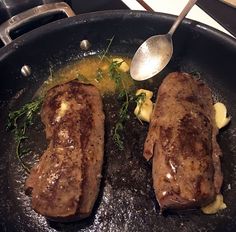 two steaks being cooked in a skillet with butter and sauce on the side