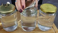 two jars filled with water and sand on top of a wooden table next to a woman's hand