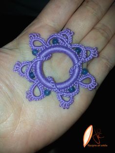 a hand is holding a small purple beaded object in it's left hand