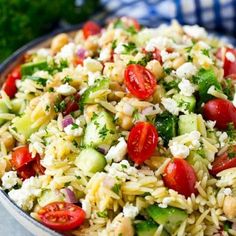 a bowl full of pasta salad with tomatoes, cucumbers and parsley