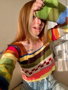 a woman with red hair wearing a multicolored knitted sweater and denim shorts