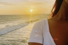 a woman standing on top of a beach next to the ocean at sun set with waves coming in