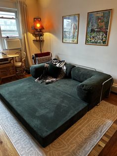 a green couch sitting on top of a wooden floor next to a lamp and window