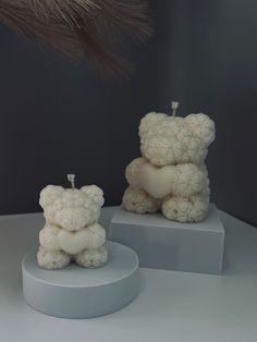 two small white teddy bears sitting on top of pedestals next to each other,