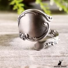 a silver ring sitting on top of a cement floor next to green plants and leaves