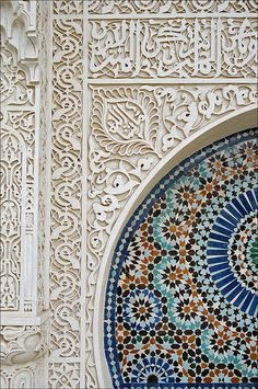 an intricately designed wall with a clock on it's side and a bird perched on top