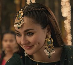 a woman wearing green and gold jewelry with pearls on her head, smiling at the camera