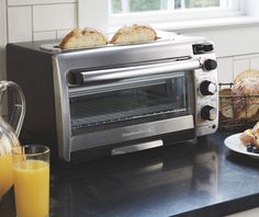 toaster oven sitting on top of a counter next to plates of bread and orange juice