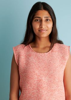 a woman standing in front of a blue wall wearing a pink top and smiling at the camera