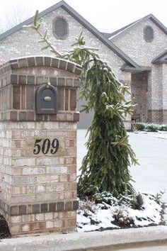 a brick mailbox sitting in the middle of a snow covered driveway next to a tree