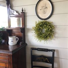 a room with a chair, mirror and wreath hanging on the wall next to a dresser