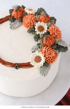 a white cake with orange flowers and leaves on top is sitting on a red tablecloth