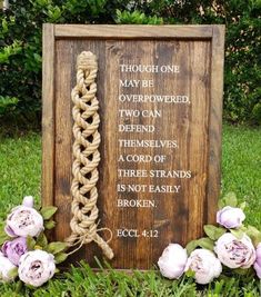 a wooden sign with rope and flowers in the grass