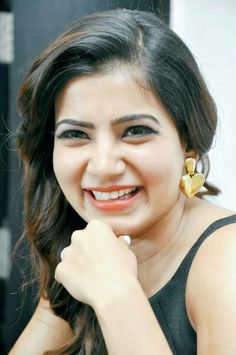 a woman with long hair smiling and holding her hand on her chin while wearing earrings