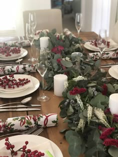 the table is set for christmas dinner with red and white flowers, greenery and candles