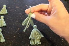 someone is holding yarn and needles to make tassels for small ornaments on the table