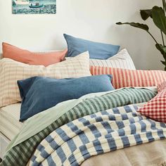 a bed topped with lots of pillows next to a potted plant on top of a table