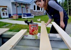 a woman standing next to a wooden fence with a can of paint on top of it