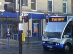 a silver and blue bus parked in front of a building next to a traffic light